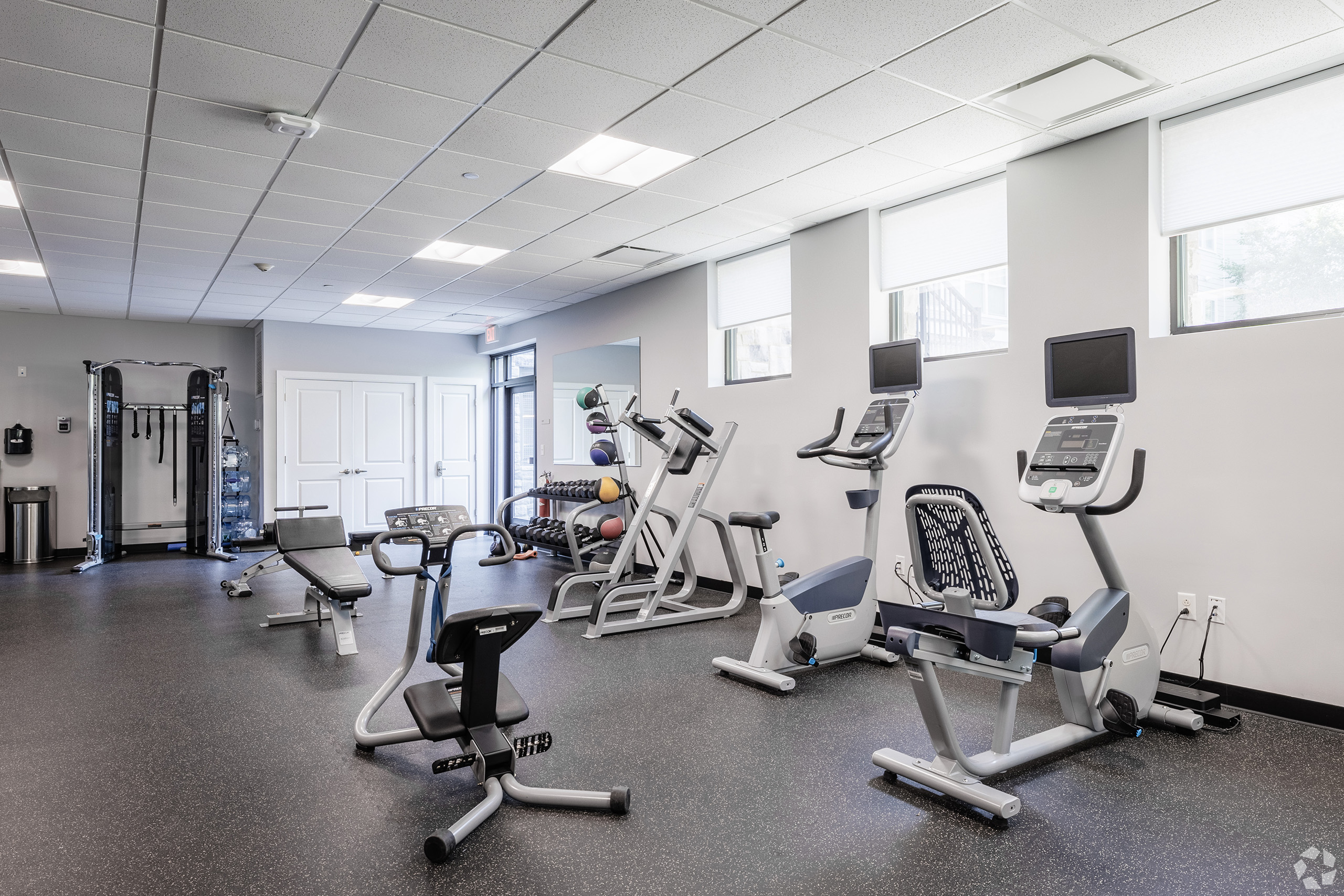 Fitness center with recumbent and upright exercise bikes featuring private TV monitors, weight bench, free weights, and a functional trainer cable machine