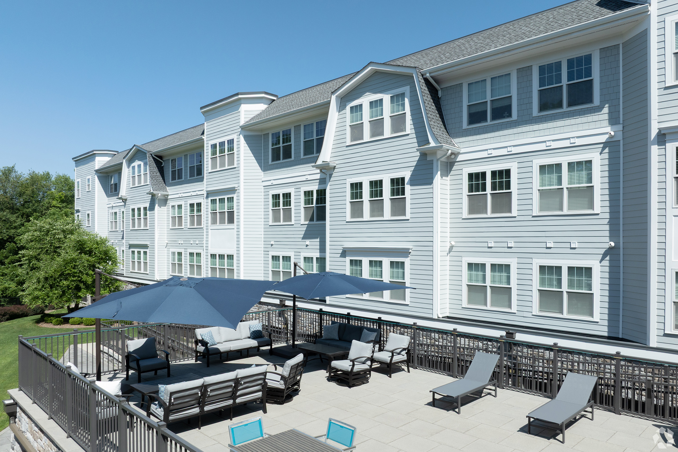 Furnished outdoor terrace with sectional seating, navy umbrellas, sun loungers, and the Colonial Pointe building exterior in the background